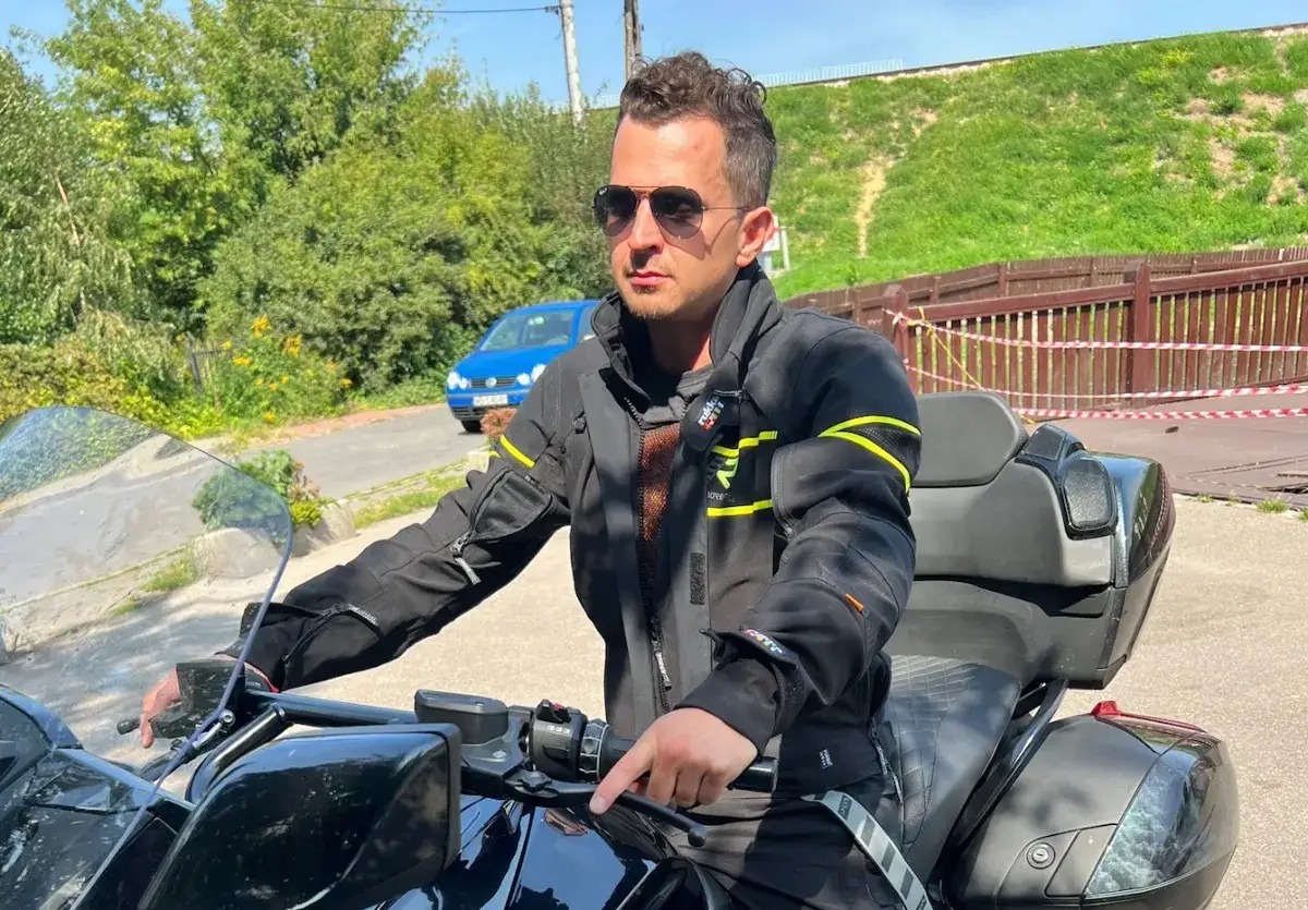 Mężczyzna w okularach przeciwsłonecznych i czarnym ubraniu na motor turystyczny, gotowy do podr&oacute;ży.