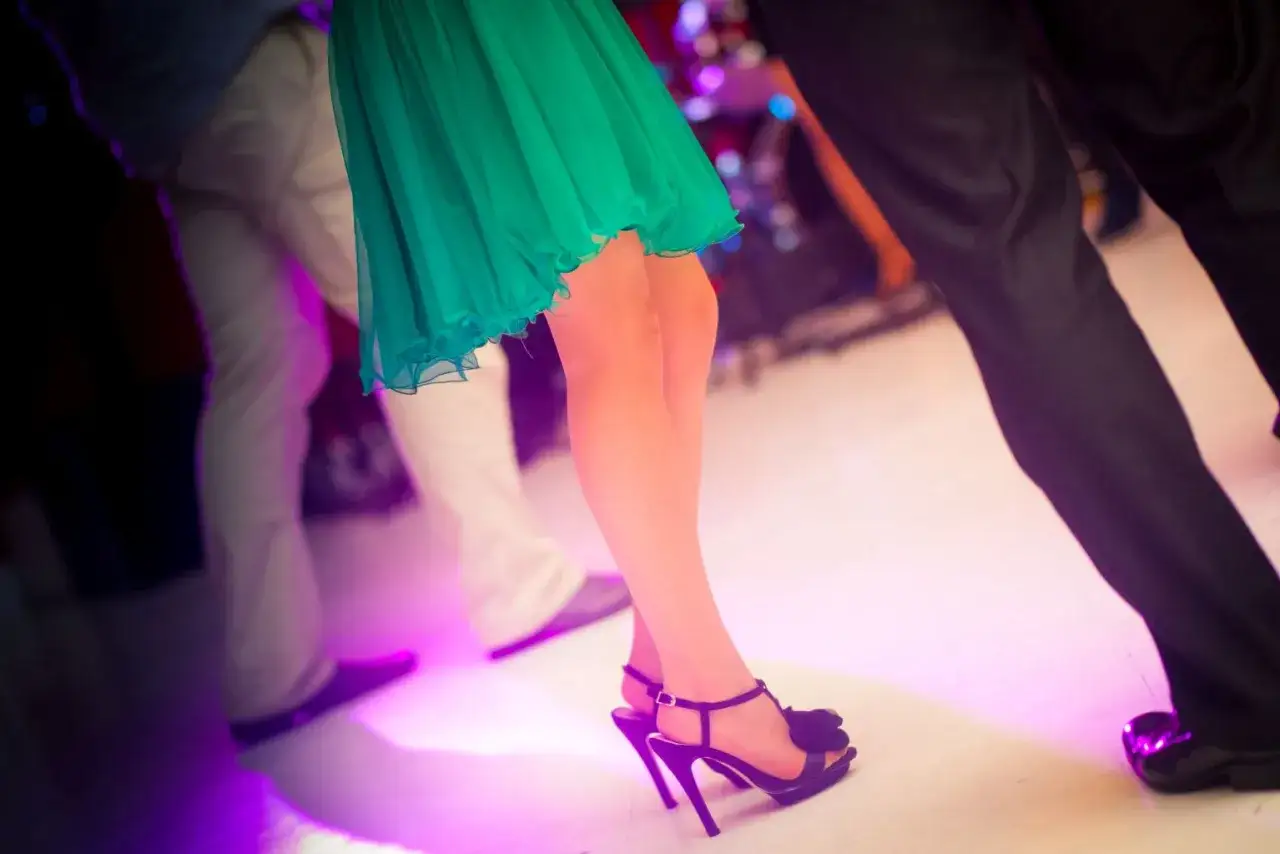 Nogi w szpilkach i zielonej sukience wirują w rytm muzyki, tworząc radosne zabawy taneczne na imprezie.