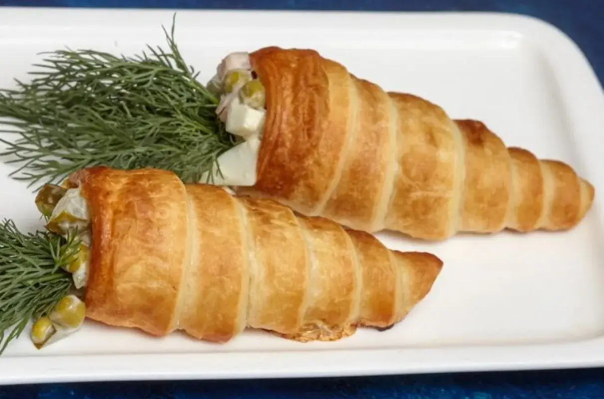 Dwa rożki z ciasta francuskiego wypełnione sałatką jarzynową i udekorowane gałązkami koperku.