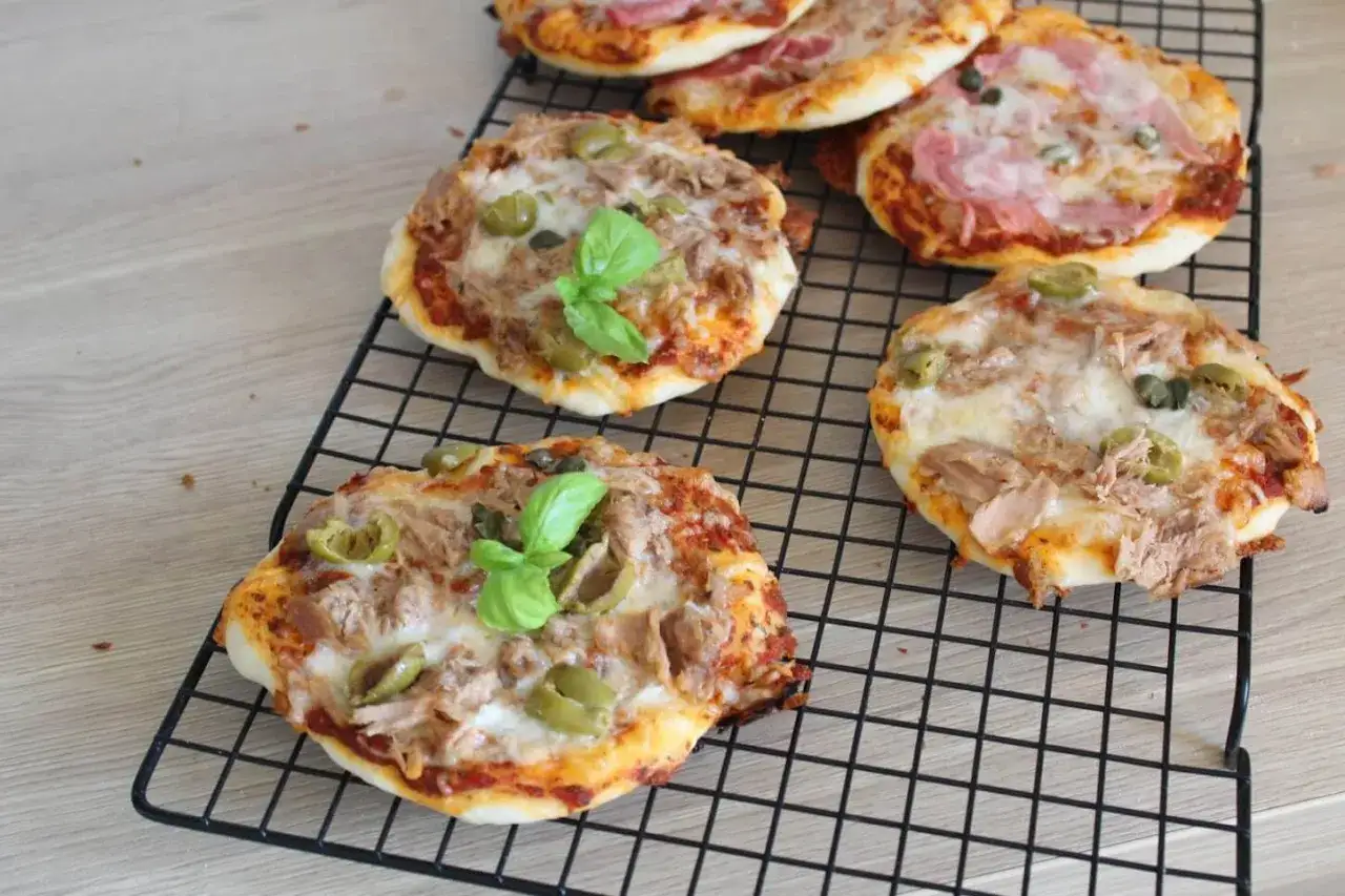 Mini pizze z tuńczykiem, oliwkami i bazylią na ruszcie, gotowe do pieczenia w piekarniku.