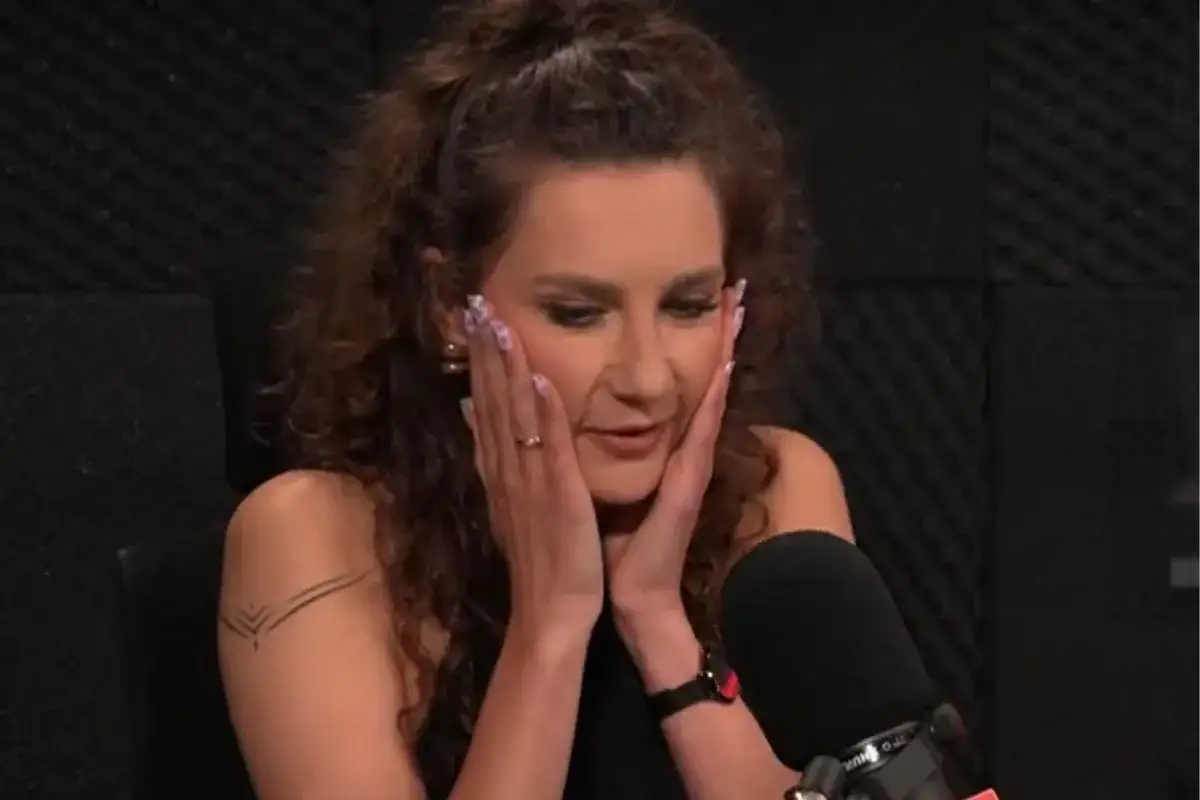 Wiola, z burzą loków i tatuażem na ramieniu, z dłońmi przy policzkach, wygląda na zaskoczoną.