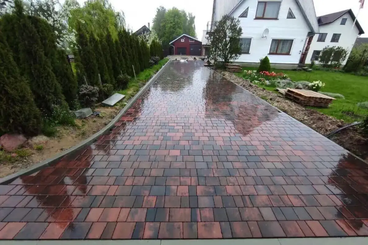 Nowy podjazd z kostki brukowej, lśniący po deszczu, prowadzi do domu.