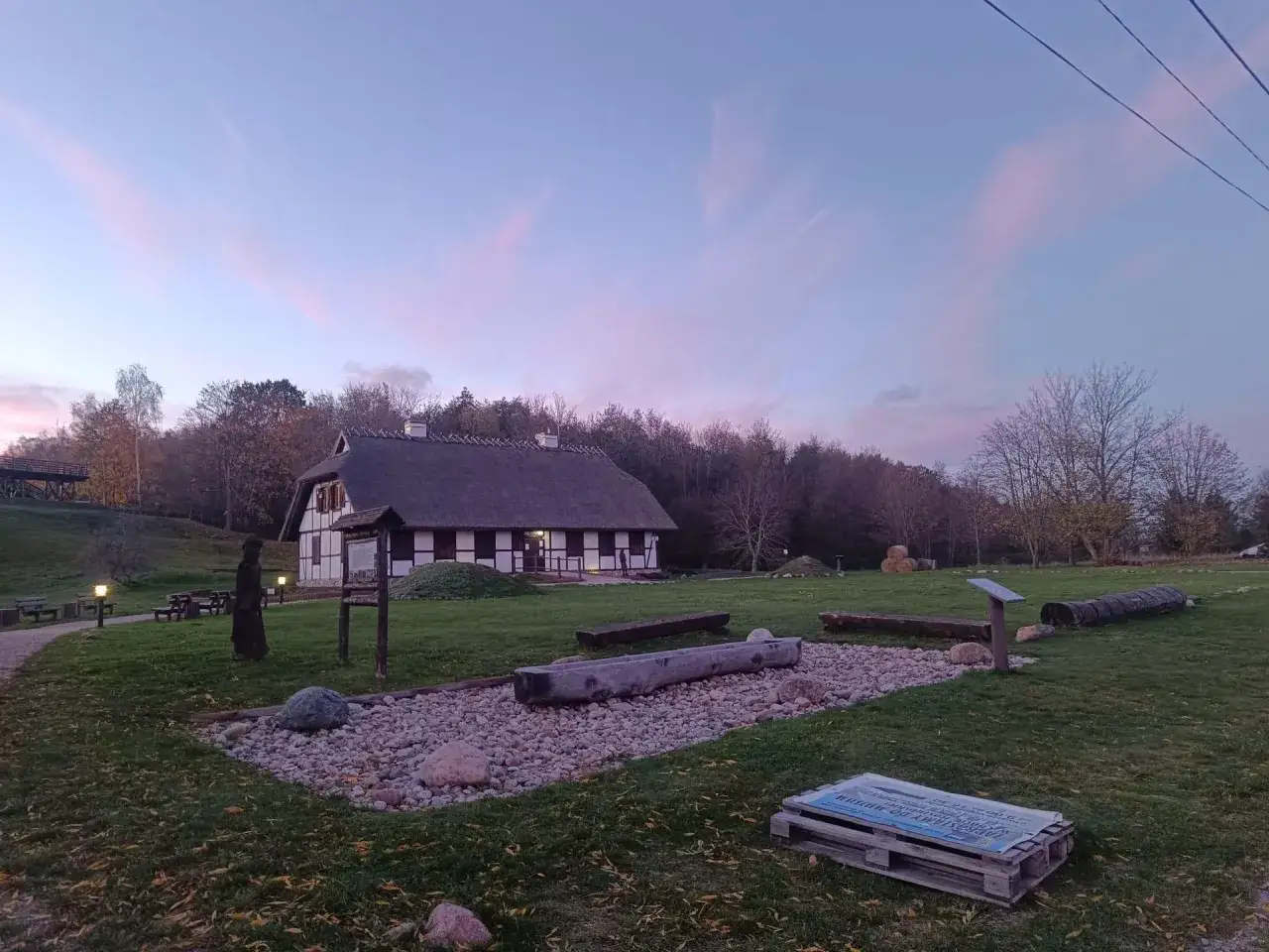 Park kulturowy osada łowców fok w Rzucewie. Dom z trzcinowym dachem i drewnianymi elementami, otoczony zielenią i kamieniami.