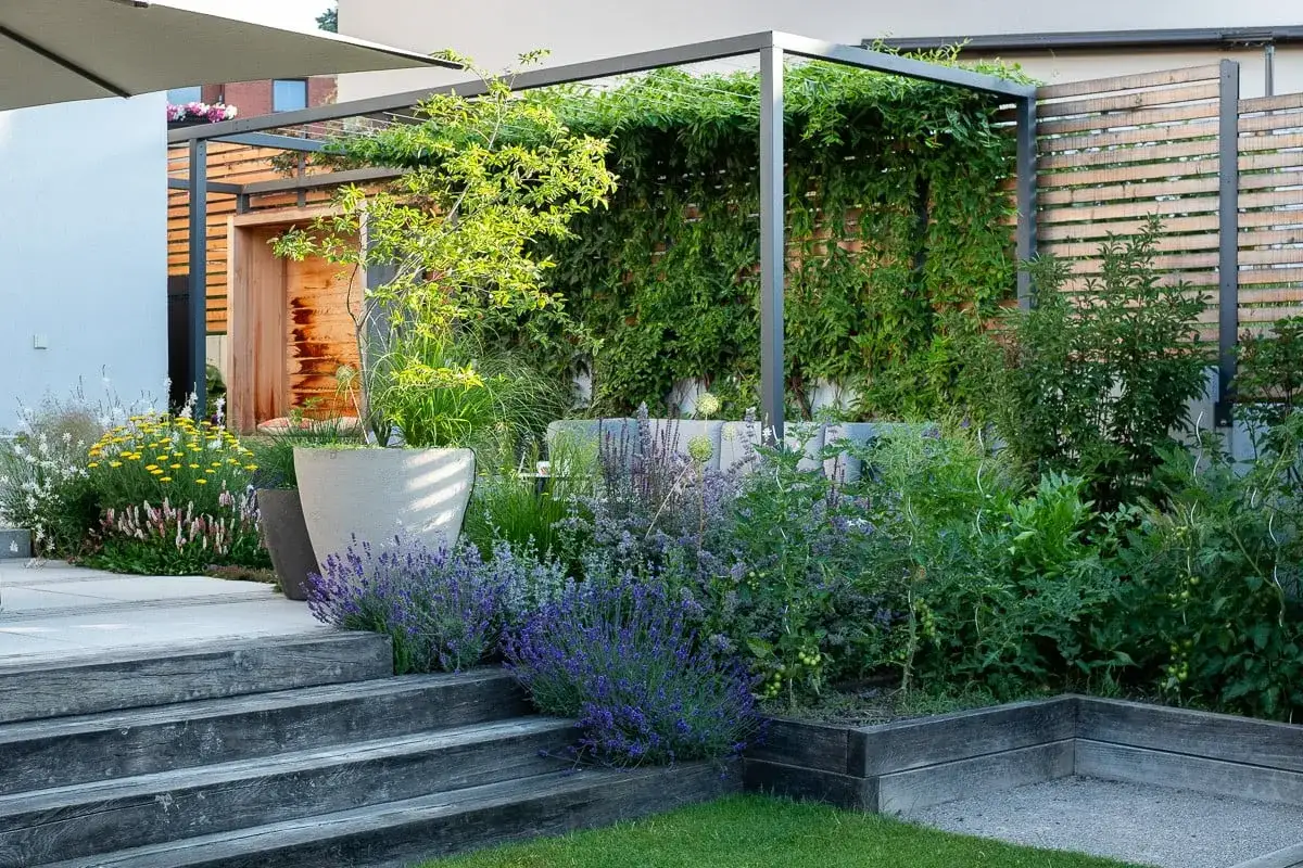 Nowoczesny pomysł na ogrodzenie ogródka: pergola z pnączami, drewniane panele i kamienne donice tworzą przytulną przestrzeń.