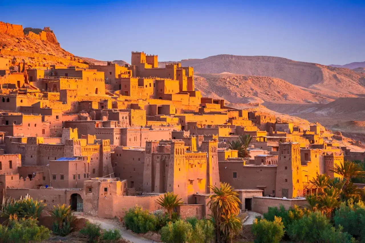 Kasba Ait-Ben-Haddou, wpisana na listę UNESCO, wznosi się na zboczu góry Atlas. Złote światło zachodzącego słońca oświetla gliniane budowle.
