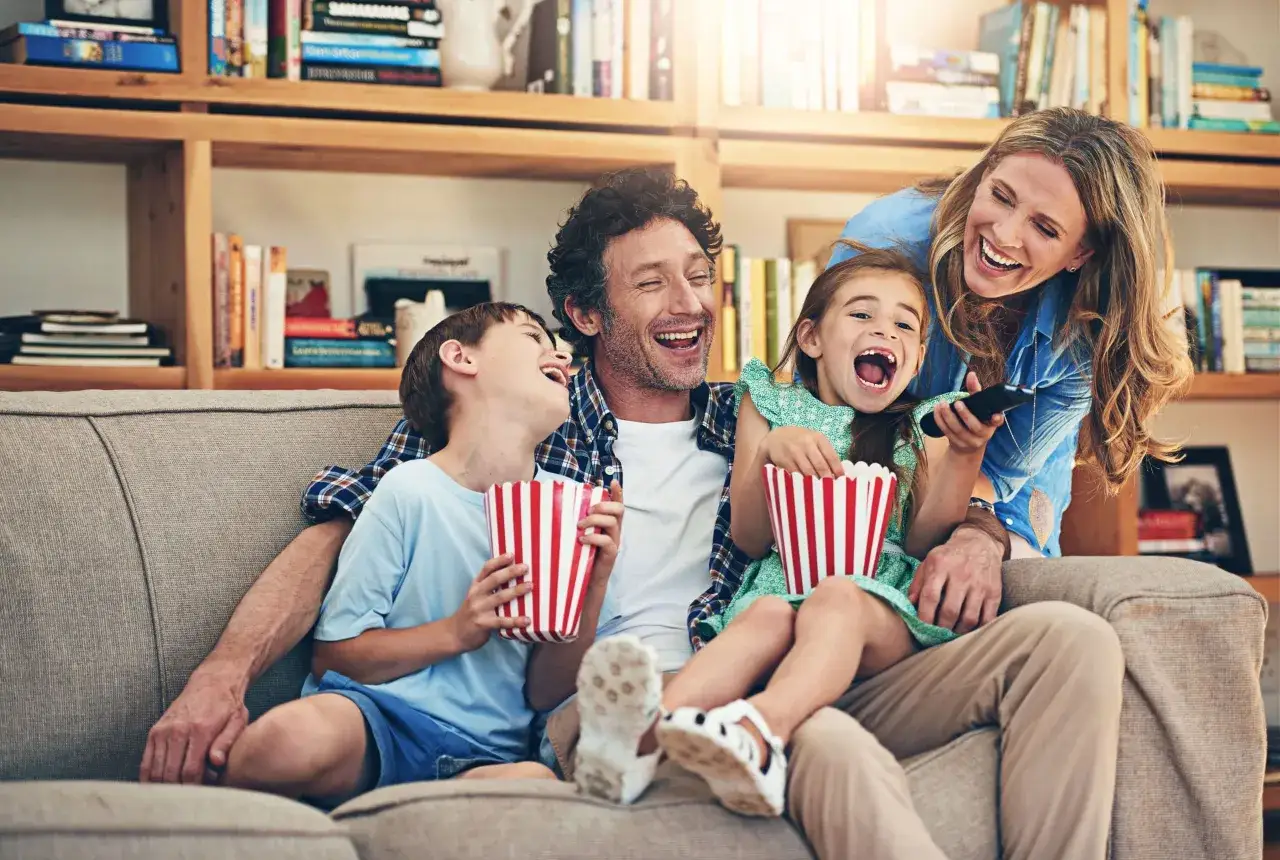 Rodzina śmieje się do łez, oglądając komedię dla dzieci. Popcorn i wspólne chwile radości.