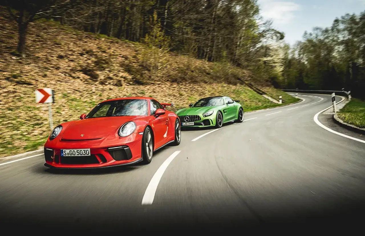 Czerwone Porsche i zielony Mercedes-AMG GTR Pro ścigają się na krętej drodze wśród drzew.
