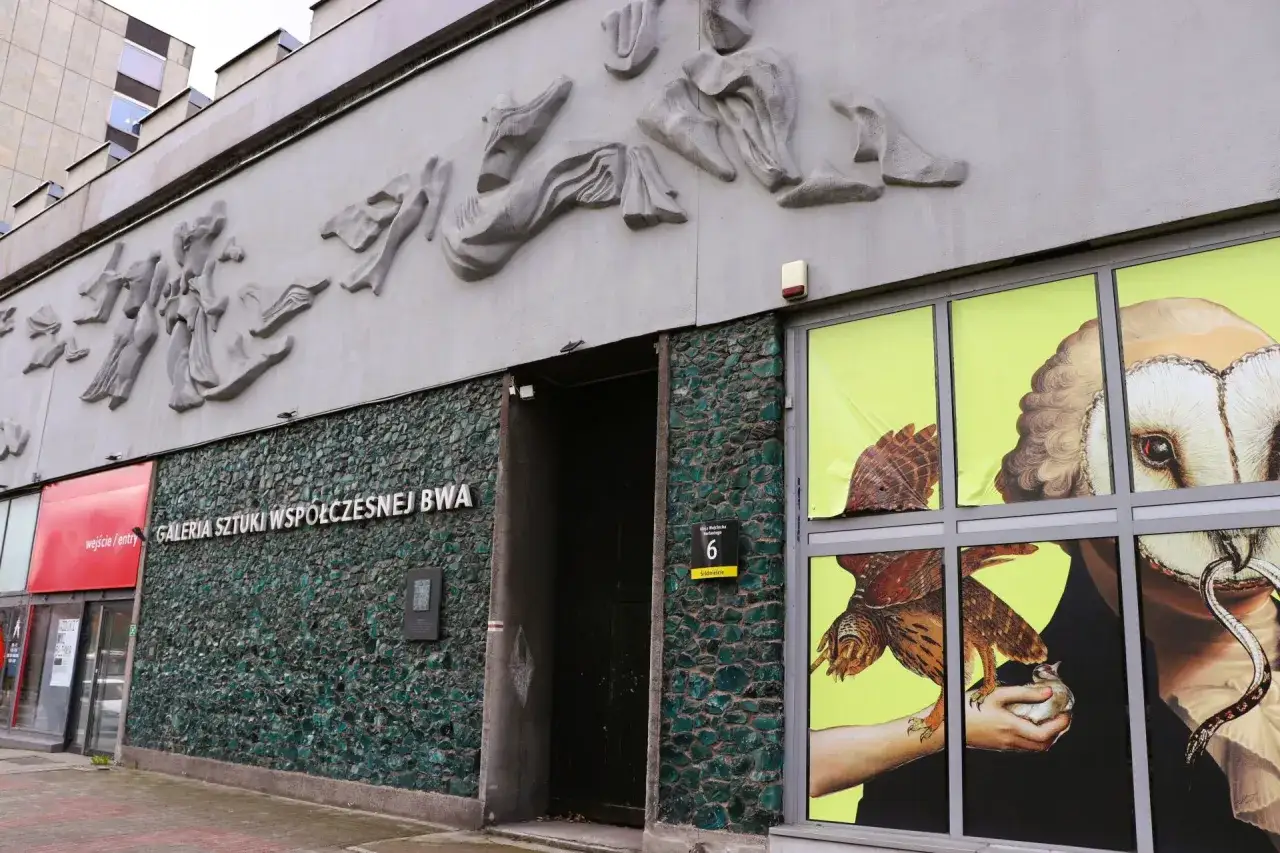 Fasada Galerii Sztuki Współczesnej BWA w Katowicach z abstrakcyjną płaskorzeźbą i witryną z grafiką sowy i ptaka.