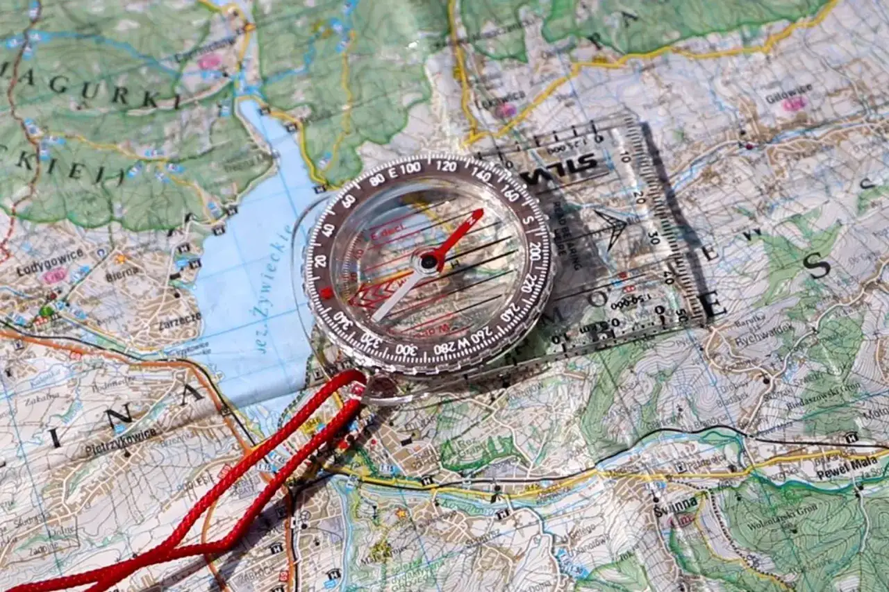 Kompas na mapie turystycznej, pokazujący, jak czytać kompas. Czerwona linka i przezroczysta linijka ułatwiają orientację w terenie.