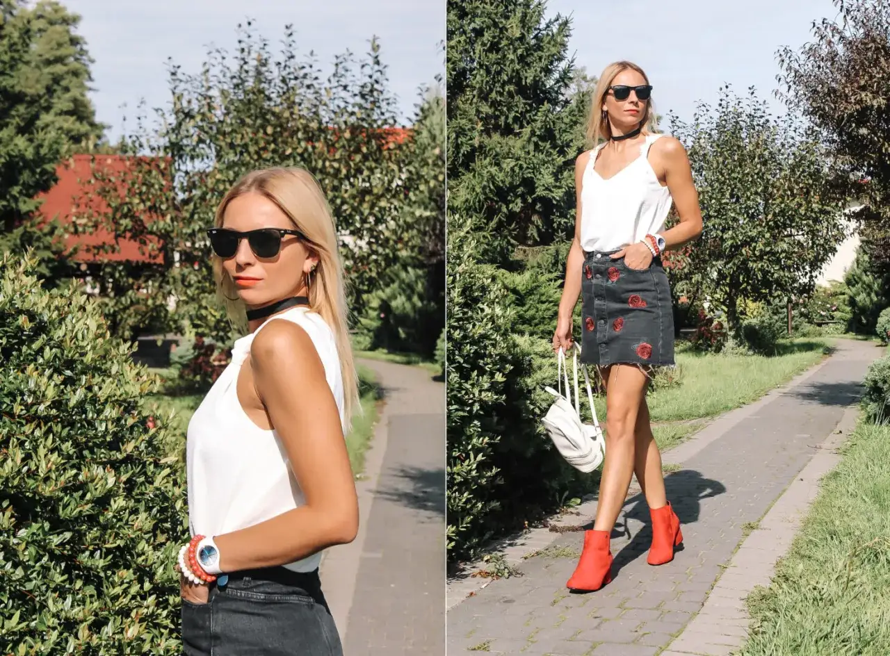 Kobieta w białej bluzce i jeansowej sp&oacute;dnicy z r&oacute;żami, w słoneczny dzień prezentuje stylowe, czerwone buty.