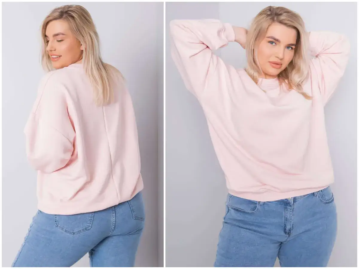 Modelka w różowej bluzie plus size i jeansach. Luźny krój bluzy zapewnia komfort i swobodę ruchów.