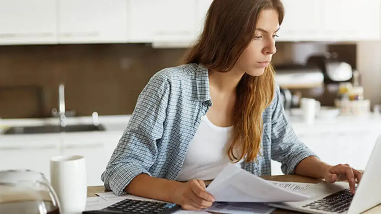 Kobieta analizuje dokumenty i szuka informacji, jak przedłużyć termin spłaty pożyczki, siedząc przy laptopie w kuchni.