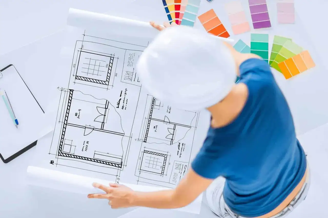 Osoba w kasku analizuje plany architektoniczne, wybierając kolory z próbnika. To kluczowy etap w urządzeniu pokoju.