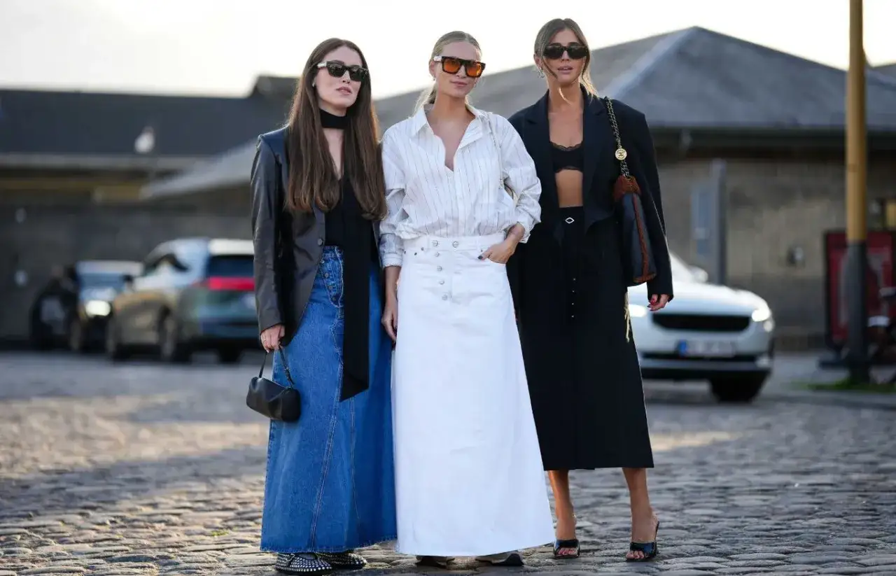 Trzy kobiety prezentują stylowe stylizacje ze sp&oacute;dnicą: jeansową maxi, białą denimową i czarną oł&oacute;wkową.