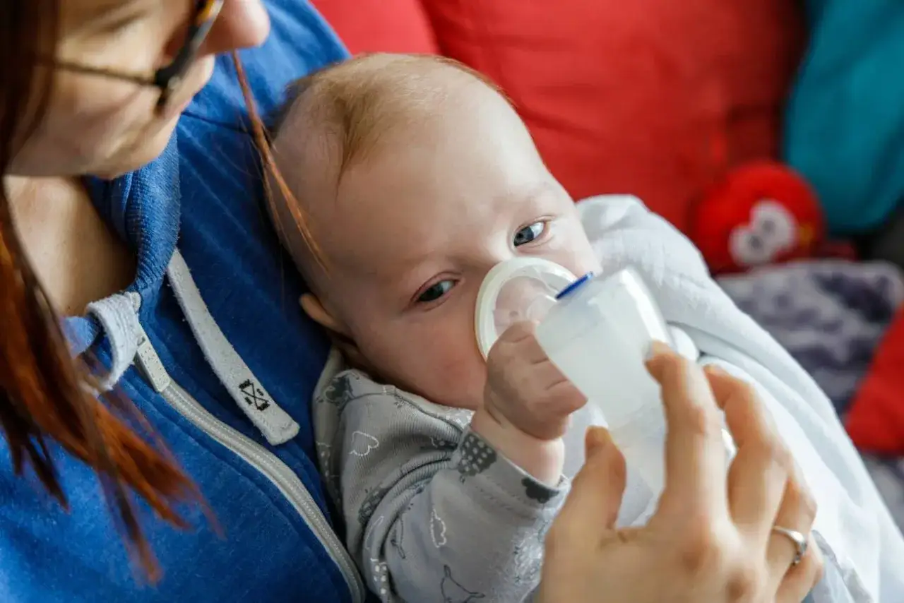 Mama podaje dziecku inhalator, by pomóc mu w walce z objawami wirusa.
