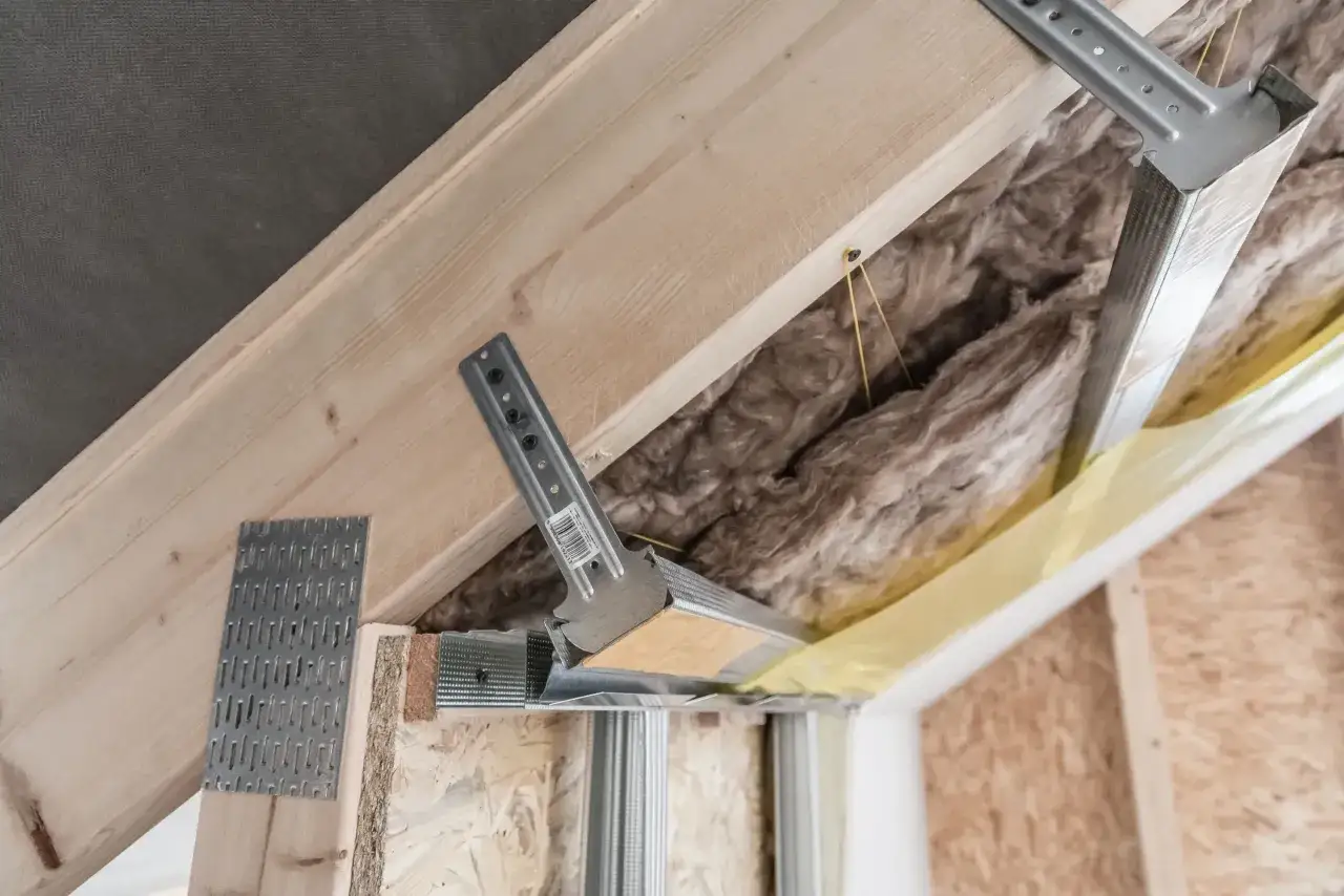 Konstrukcja podwieszanego sufitu z wełną mineralną. Widać metalowe profile i drewniane elementy, a także mocowania. Pytanie: jakie wkręty do wieszak&oacute;w grzybkowych?