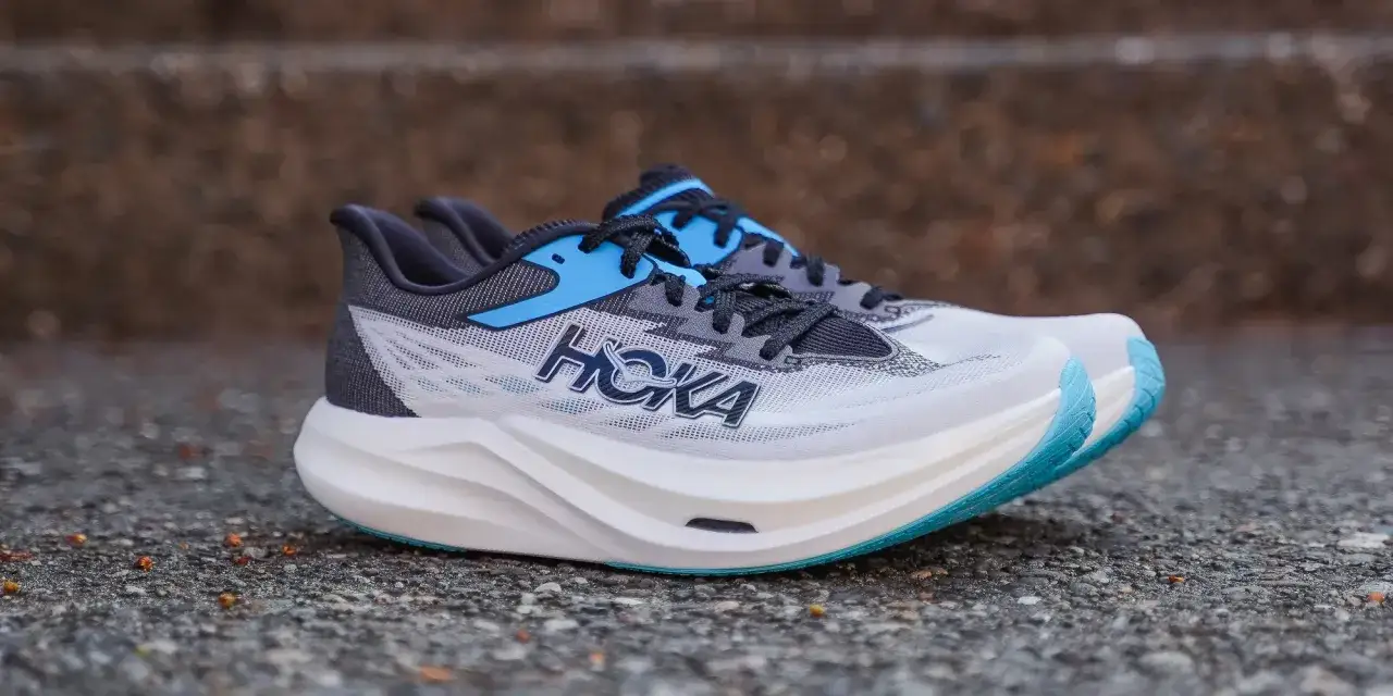 Białe buty do biegania Hoka z niebieskimi akcentami i charakterystycznym logo. Hoka to firma znana z innowacyjnych podeszw.