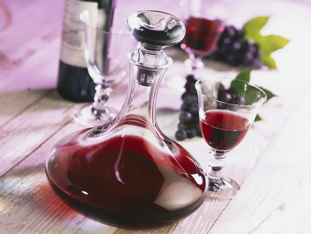 Kieliszek i karafka wypełnione rubinową nalewką z winogron, obok kiście ciemnych winogron.