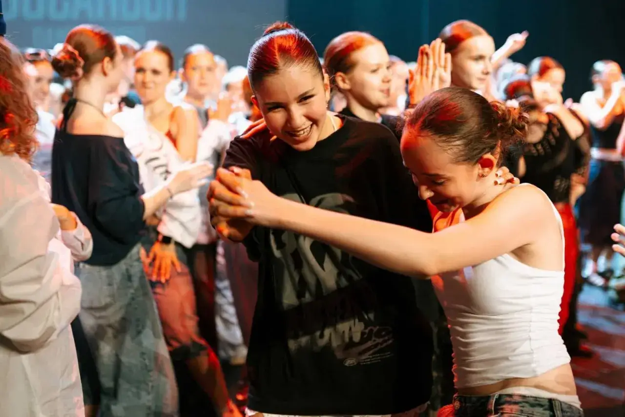 Radość na twarzach dziewcząt podczas nauki tańca towarzyskiego. W tle widać innych uczestników.