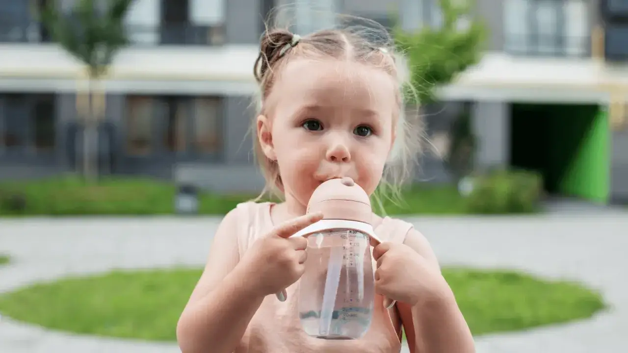 Mała dziewczynka pije z butelki, uważaj na próchnicę butelkową u 2 latka.