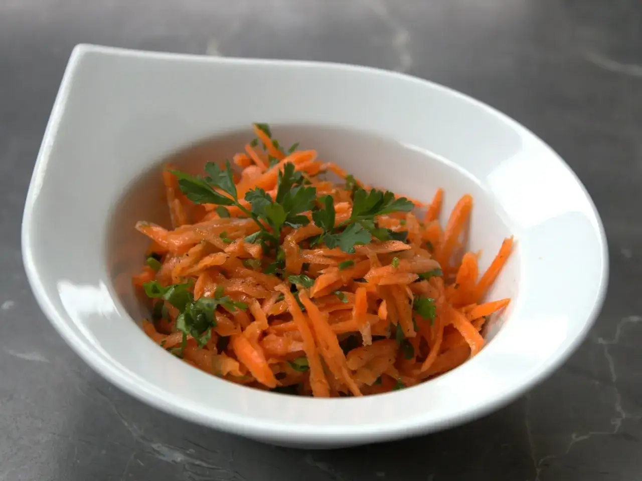 Wykwintna surówka z marchewki jak z restauracji, udekorowana świeżą natką pietruszki, podana w eleganckiej białej miseczce.