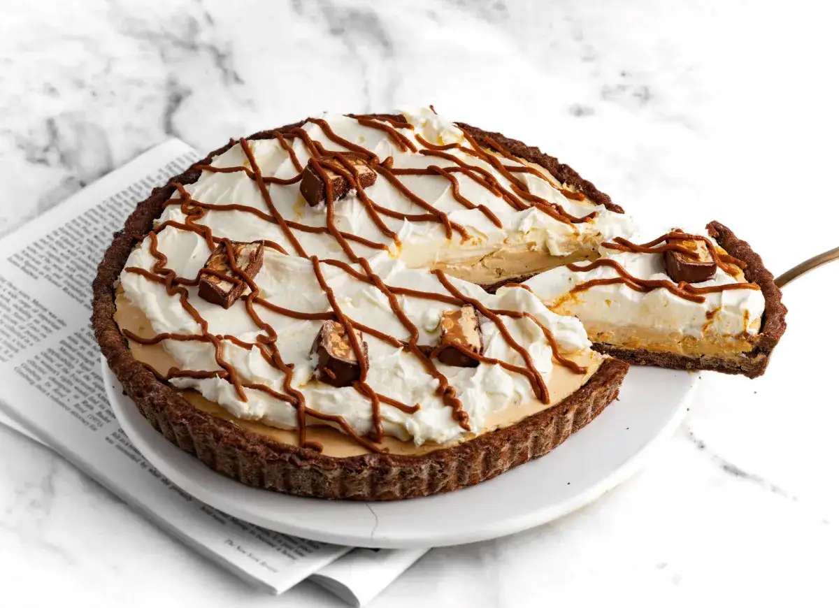 Pyszna tarta z kajmakiem i mascarpone, udekorowana bitą śmietaną, polewą karmelową i kawałkami batoników.