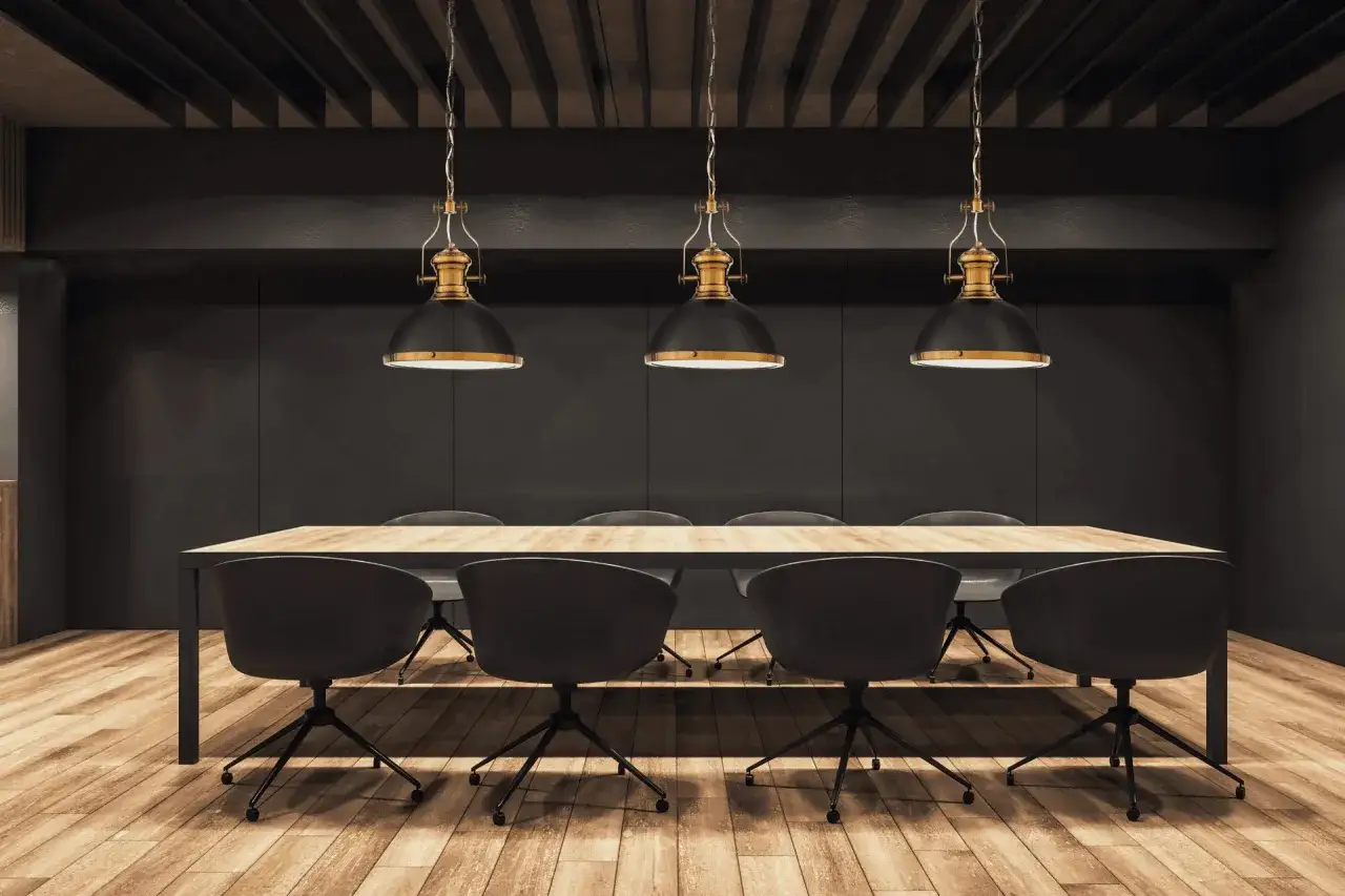 Elegancka sala konferencyjna z drewnianą podłogą, dużym stołem i trzema wiszącymi lampami. Każda lampa czarna z drewnem, w stylu industrialnym, tworzy przytulną atmosferę.