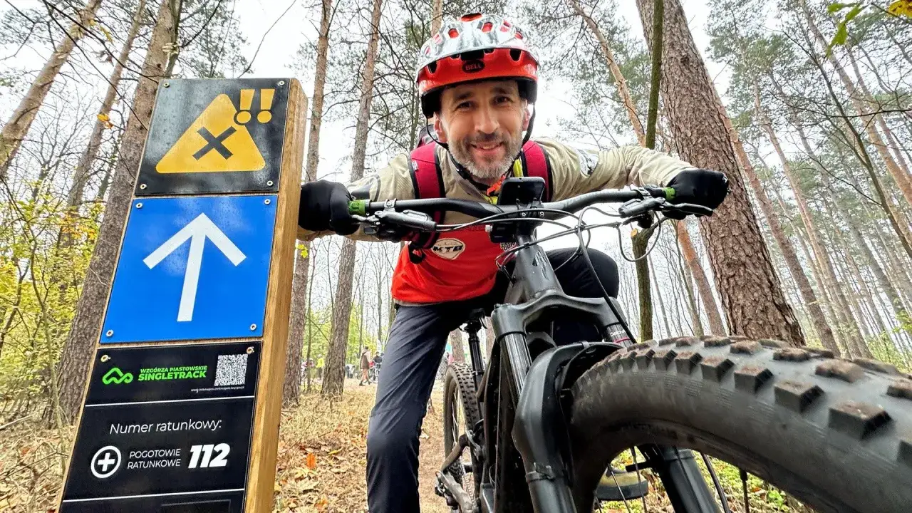 Uśmiechnięty rowerzysta na tle znaku szlaku singletrack w lesie.