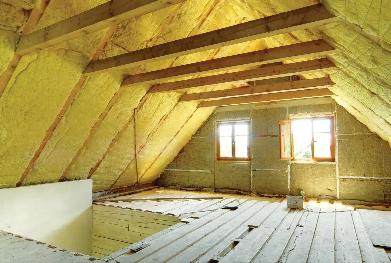 Izolacja poddasza to kluczowy etap, jak zrobić sufit na poddaszu. Widoczne drewniane belki i ż&oacute;łta wełna mineralna.