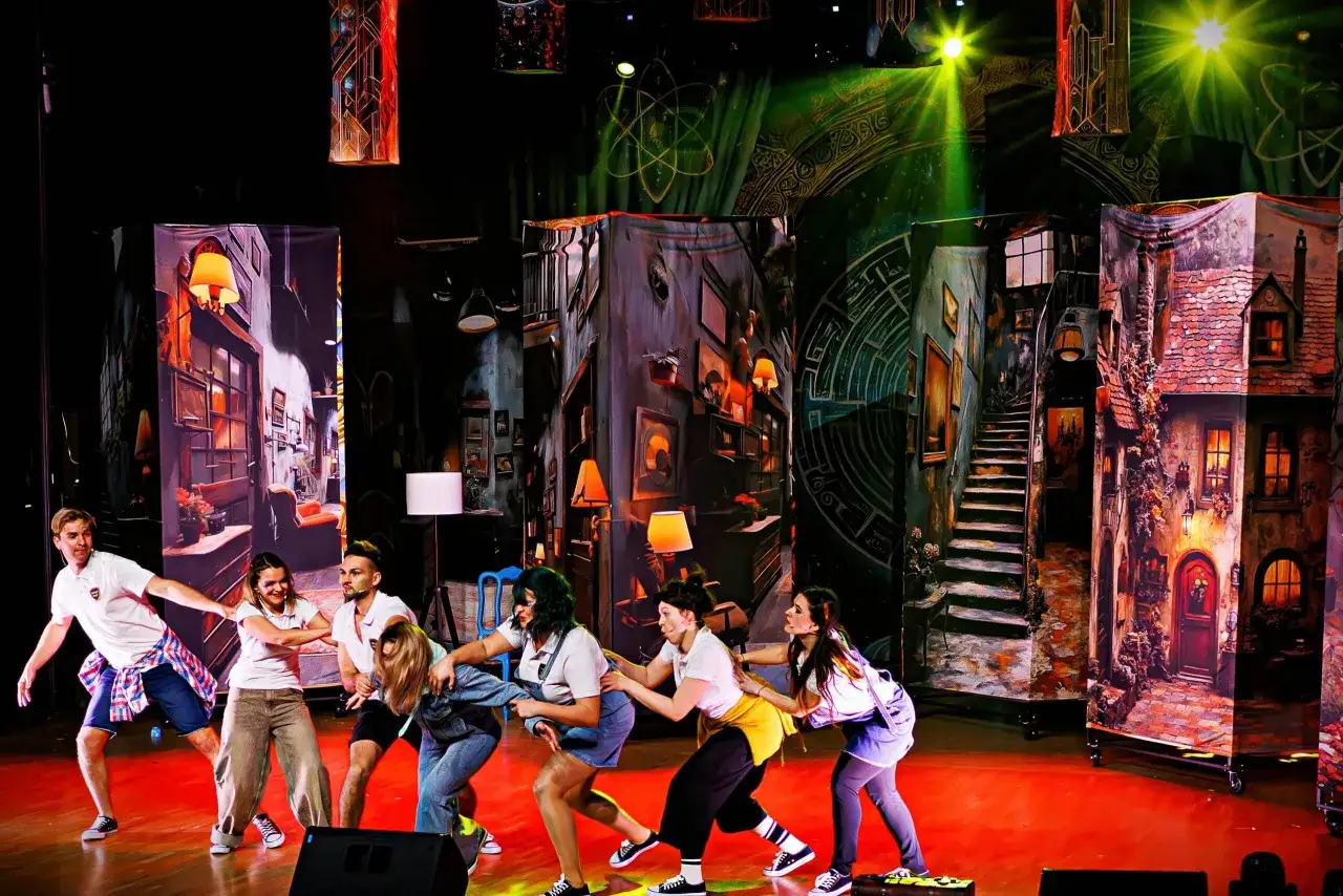 Grupa młodych aktorów na scenie, przygotowująca się do spektaklu. To teatr dla nastolatków, gdzie scenografia przenosi widzów do magicznego świata.