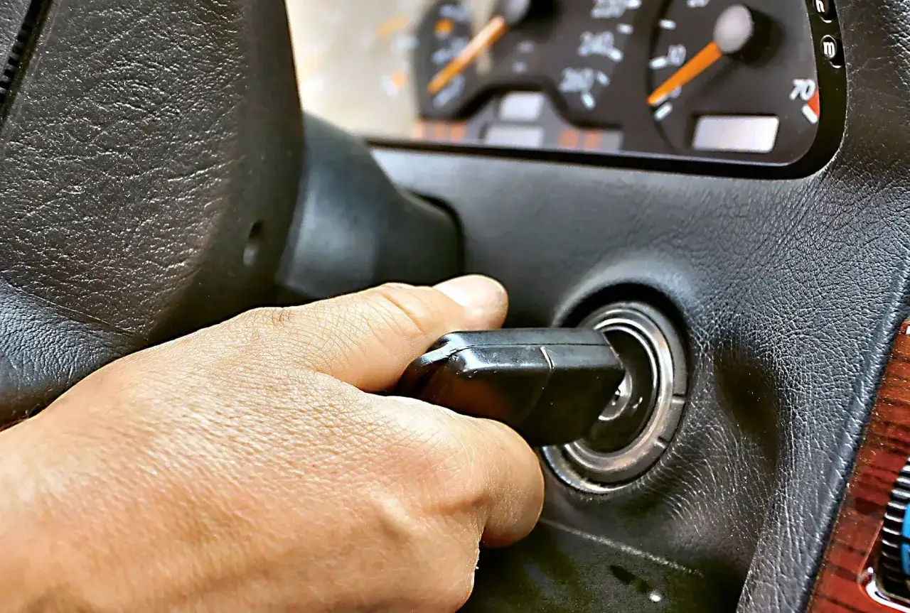 Dłoń przekręca kluczyk w stacyjce. Samochód odpala i gaśnie benzyna, co sugeruje problem z paliwem.