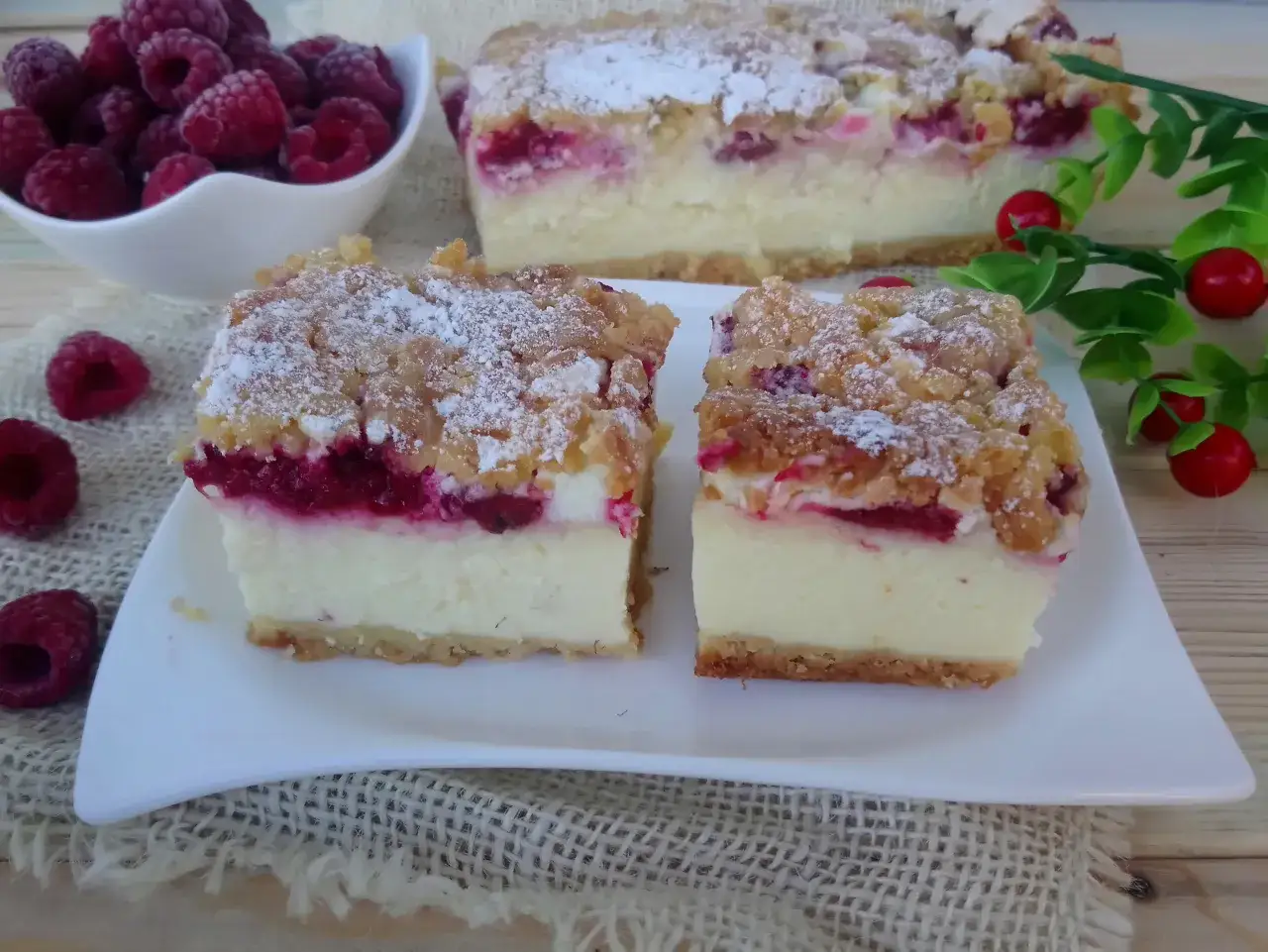 Pyszny sernik z jogurtów greckich z malinami i kruszonką, posypany cukrem pudrem.