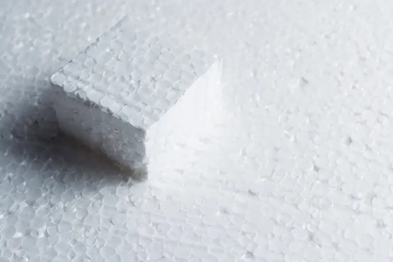 Biały klocek styropianu na tle drobnych kuleczek. Zastanawiasz się, czym wypełnić dziury w styropianie?