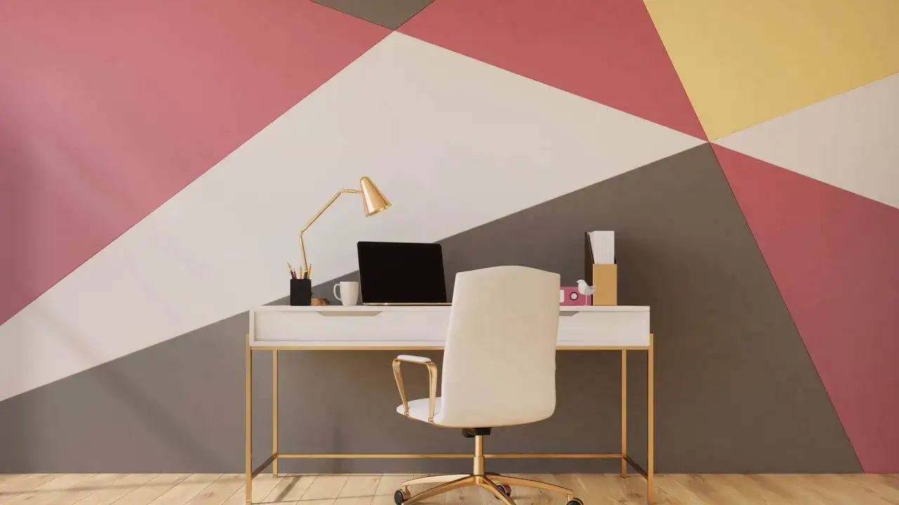 Biurko z laptopem i lampką na tle ściany z geometrycznymi, kolorowymi panelami. Malowanie ścian ciekawe wzory dodaje wnętrzu charakteru.