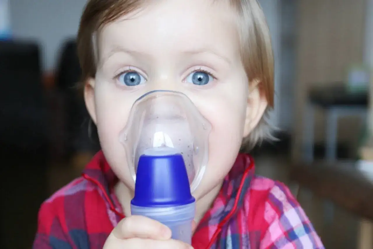 Małe dziecko z niebieskimi oczami używa nebulizatora, by leczyć zapalenie oskrzeli.