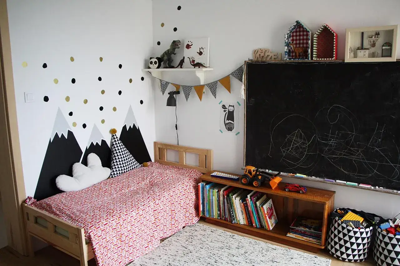 Pokój dla chłopca 4 lata: łóżko z kolorową pościelą, góry na ścianie, tablica kredowa i zabawki.