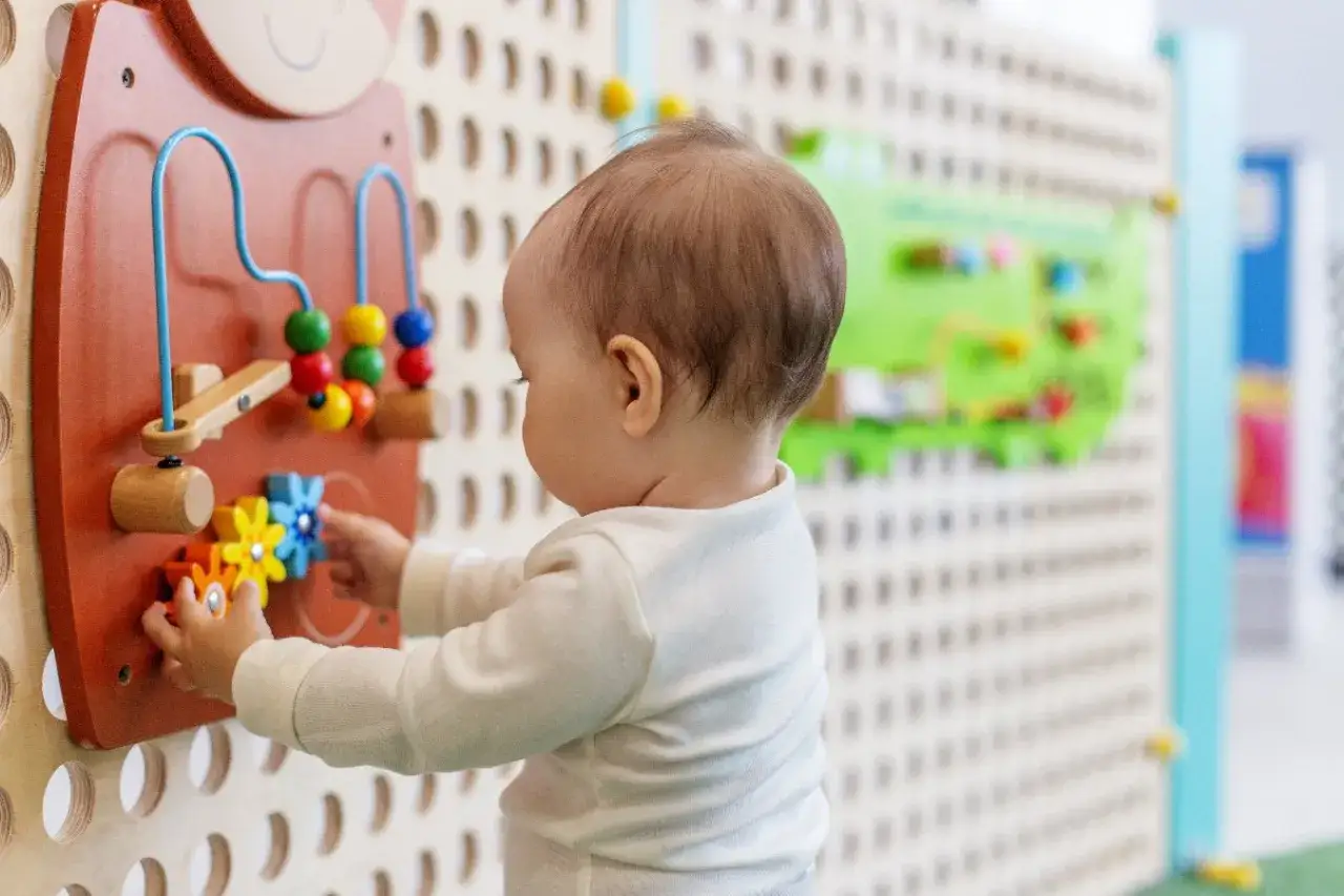 Maluch odkrywa świat, kiedy do żłobka. Rączki bawią się kolorowymi kółeczkami na tablicy interaktywnej.