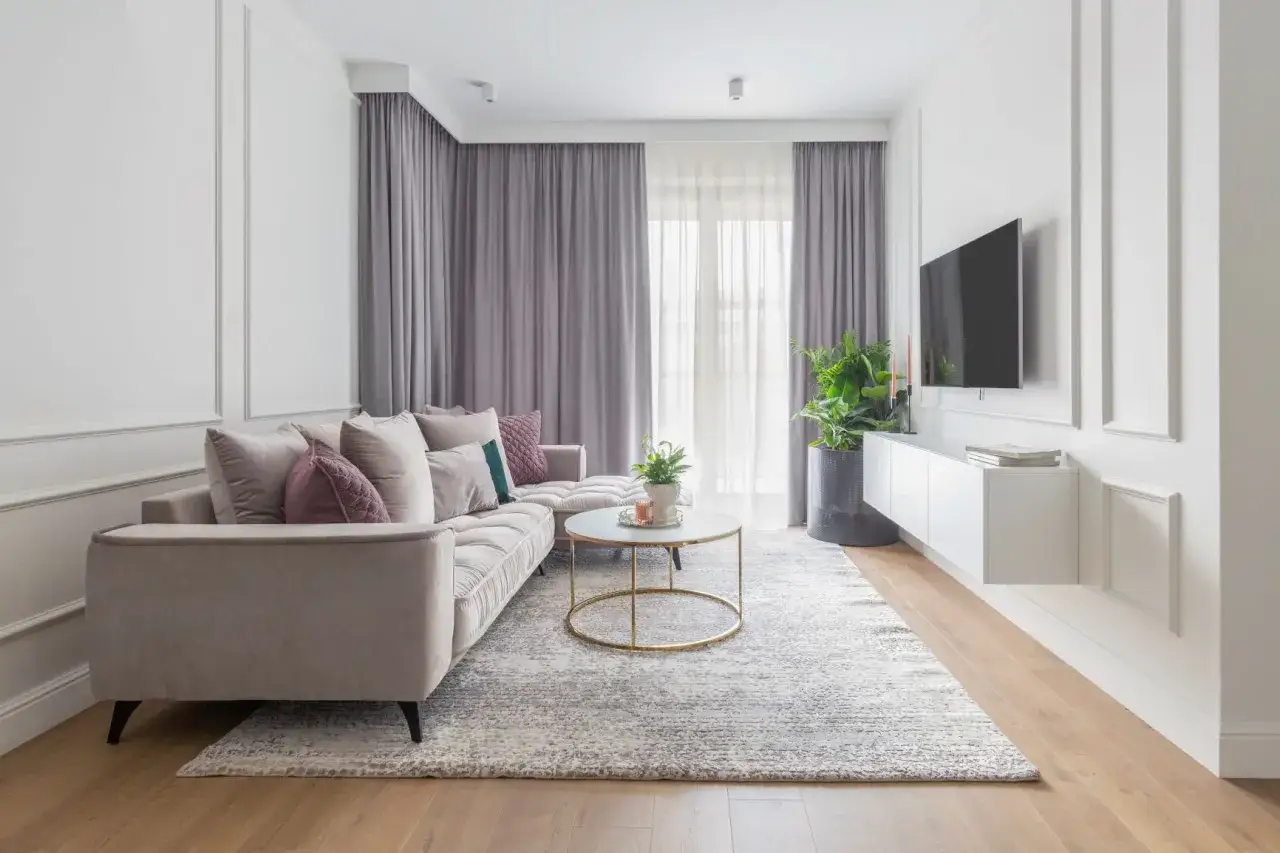 Elegancki salon w stylu modern classic z beżową sofą, złotym stolikiem kawowym i szarymi zasłonami.