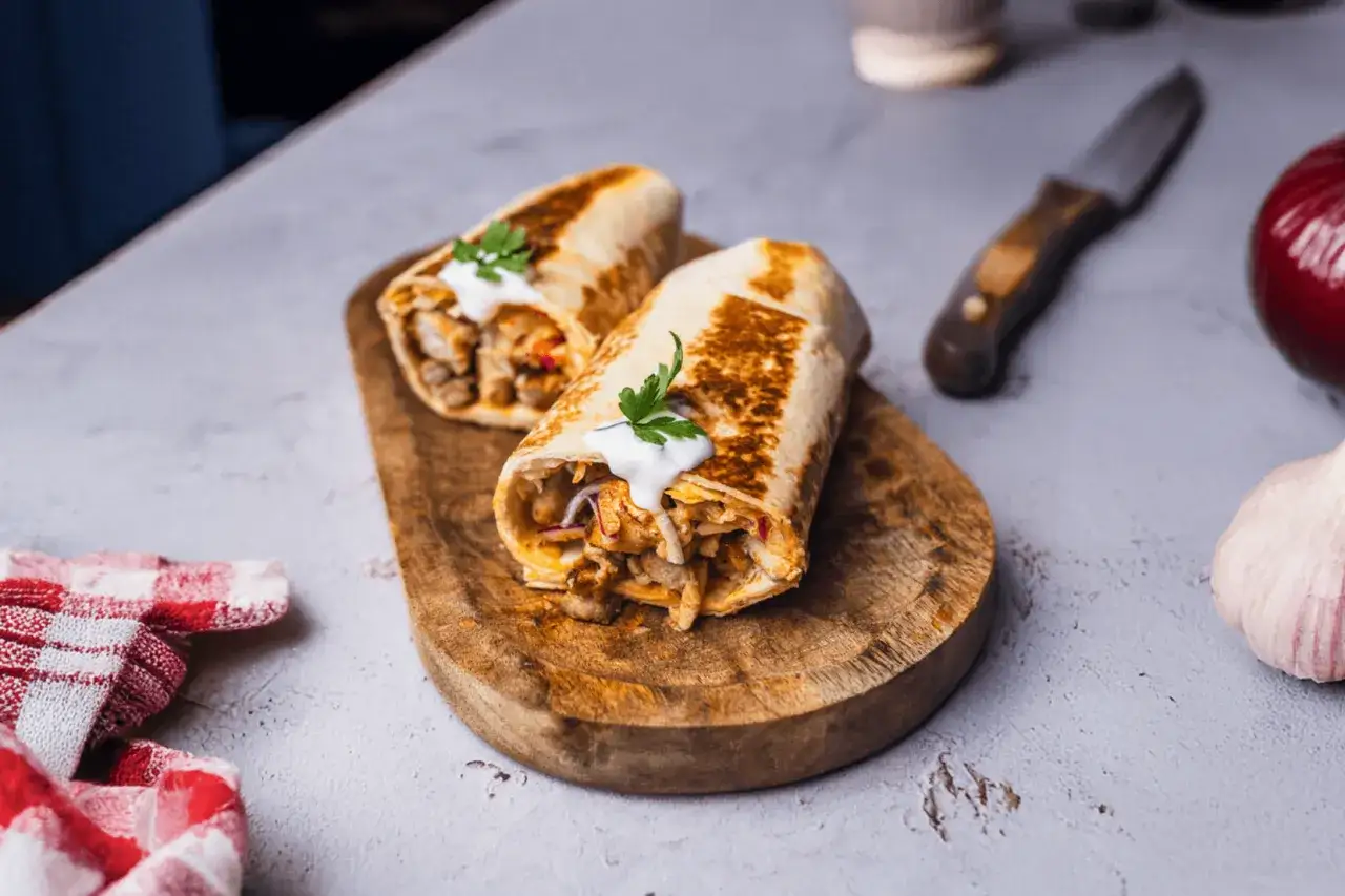 Dwa sycące kebaby w cieście, polane sosem, na drewnianej desce. Zastanawiasz się, ile kalorii ma kebab w cieście?