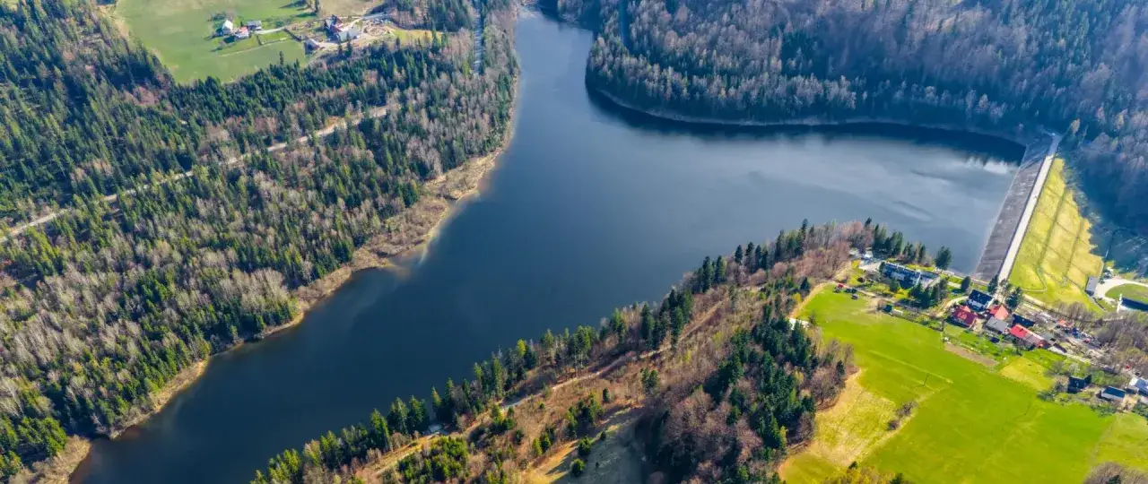 Malownicze jezioro Czerniańskie otoczone lasami, z widoczną zaporą i zabudowaniami na brzegu.