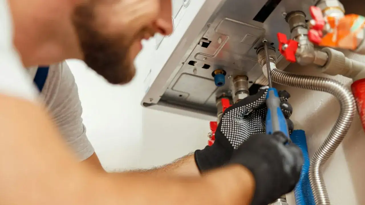 Technik dokręca śrubę przy piecu gazowym, przygotowując go do sezonu grzewczego. Sezon grzewczy zazwyczaj trwa od października do kwietnia.
