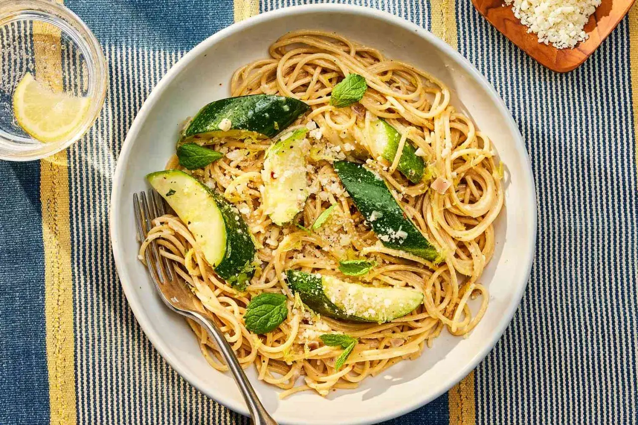 Pyszny makaron z cukinii, posypany parmezanem i świeżą miętą, podany na talerzu z widelcem.