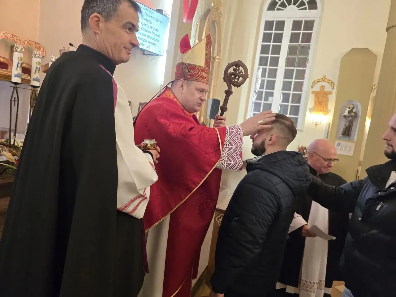 Biskup udziela sakramentu bierzmowania dorosłemu mężczyźnie. Warto wiedzieć, ile kosztuje bierzmowanie dla dorosłych, by przygotować się duchowo i materialnie.