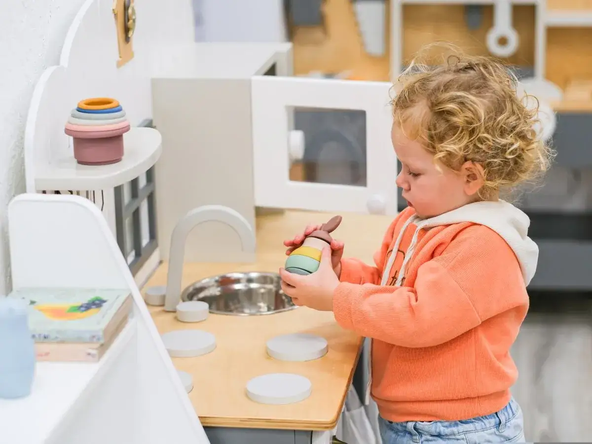 Mała dziewczynka z kręconymi włosami bawi się w kuchni, jakby przygotowywała się do żłobka.