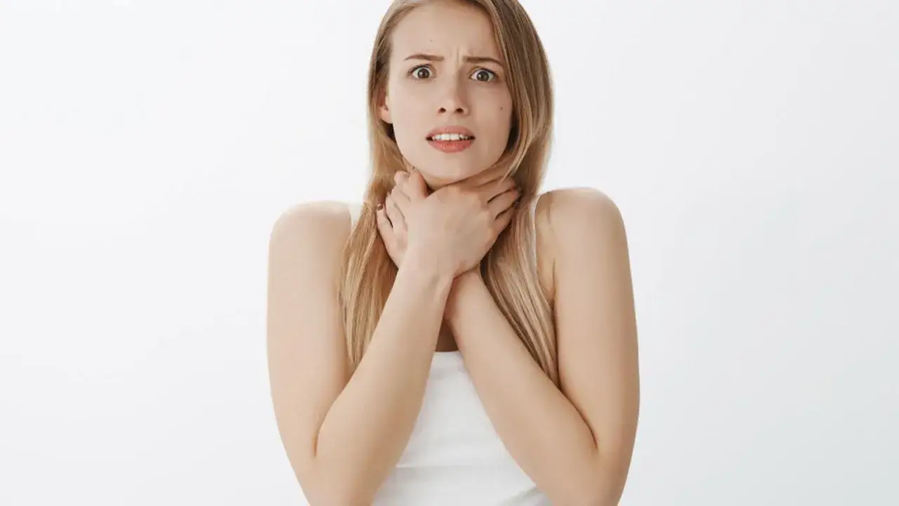 Przerażona kobieta z rękami na szyi, odczuwająca globus histericus.