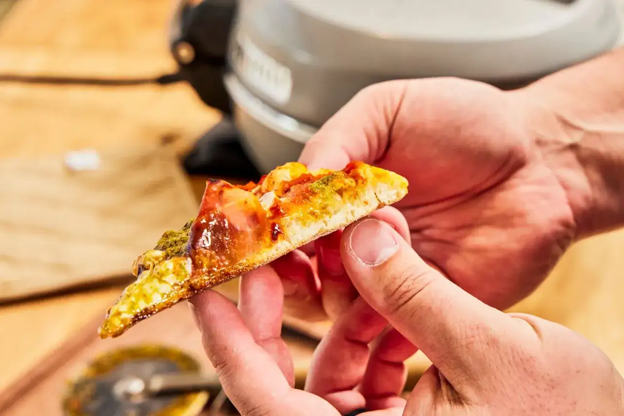 Kawałek pysznej pizzy z szynką i pesto, idealnie wypieczonej w piecu z termoobiegiem.