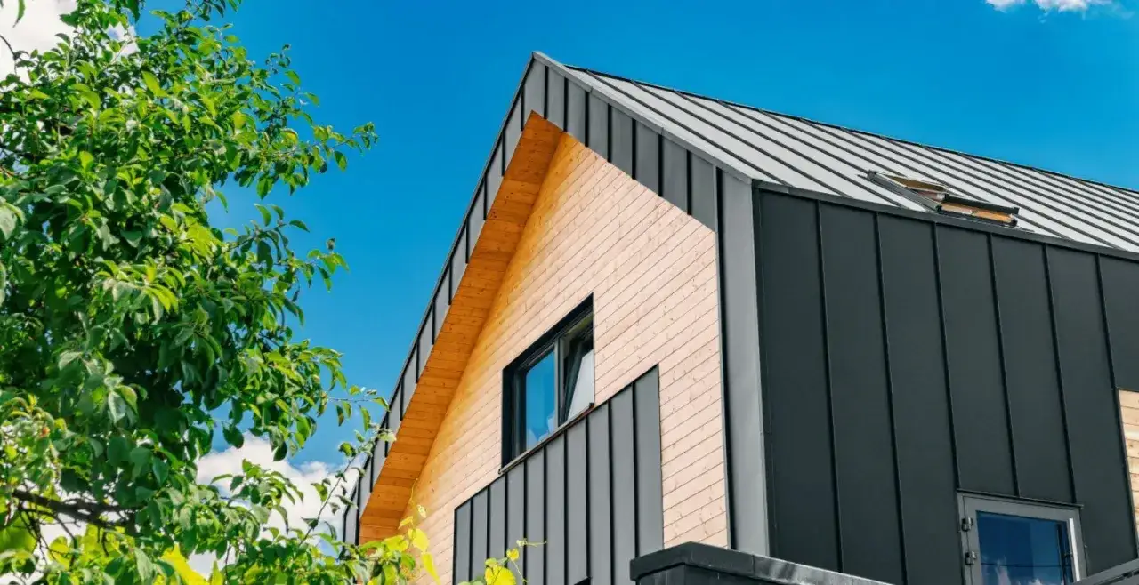 Nowoczesny dom z drewnianą elewacją i ciemną blachą na rabek, otoczony zielenią.