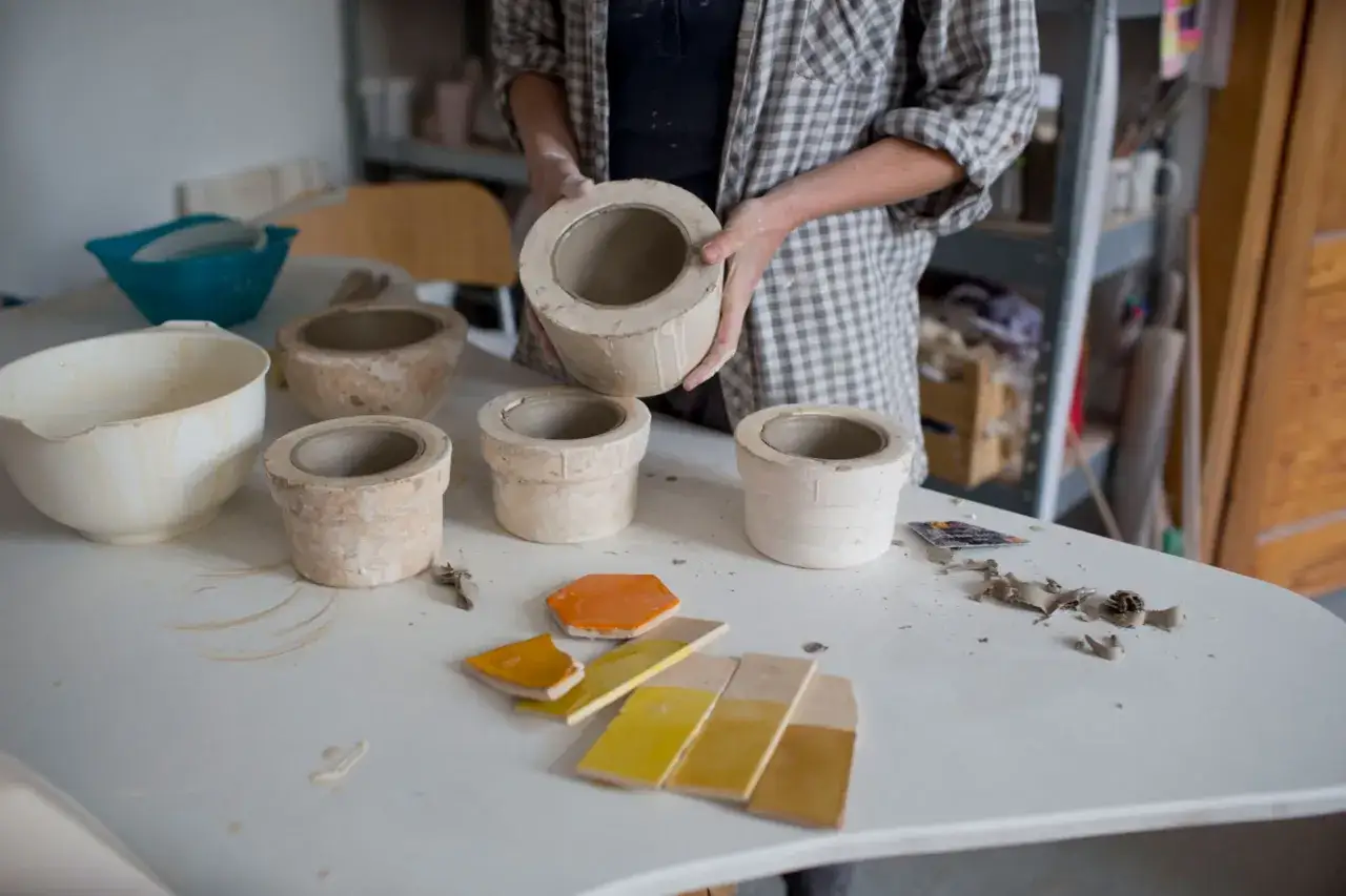 Osoba tworzy formę gipsową do ceramiki, prezentując gotowe elementy na stole.