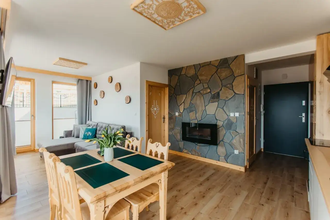 Przytulny apartament Wierchy Zakopane z kamiennym kominkiem, drewnianym stołem i widokiem na góry.