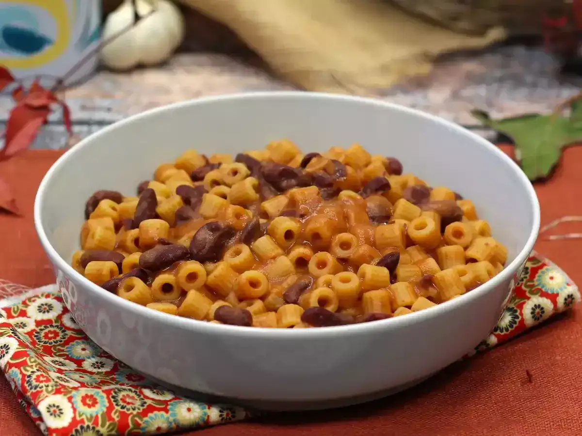 Pyszne danie Pasta e Fagioli przepis. Makaron z fasolą w sosie pomidorowym, podany w białej misce na ozdobnej serwetce.